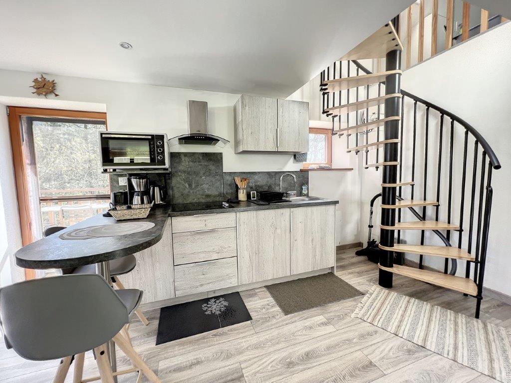 Cuisine équipée, table haute et escalier en colimaçon vers la chambre